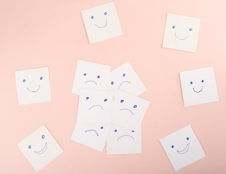 White sheets with sad and happy emotions on a pink background.の写真素材