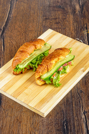 Cutting board with croissants stuffed with lettuce leaves and soft cheese, pieces of red fish and cucumbers.の写真素材