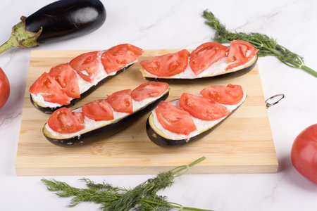 Eggplant halves with sauce and tomatoes for baking. Home cooking.の写真素材
