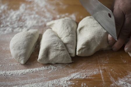 Woman cutting dough into pieces on a wooden tableの写真素材