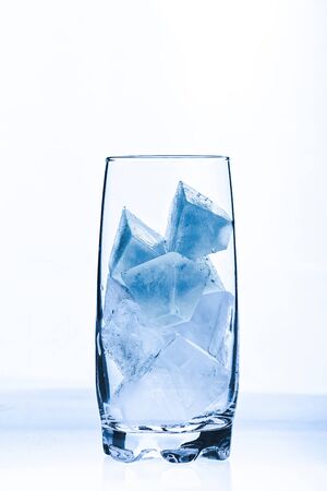 A glass with blue ice cubes against a white backgroundの写真素材