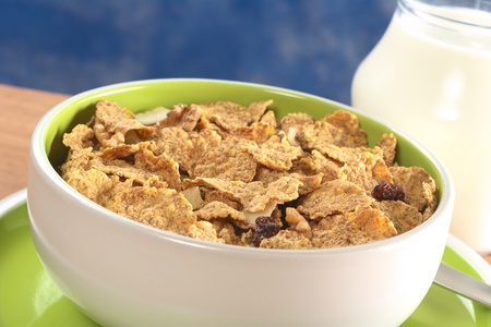 Wholewheat cereal with dried fruit, raisin and walnut in bowl and with milk in the back (Selective...