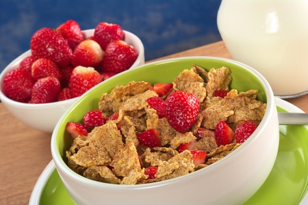 Wholewheat cereal with fresh strawberries in bowl with strawberries and milk in the back (Selective...