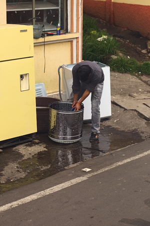 TUNGURAHUA, ECUADOR - MAY 12, 2014: Unidentified person cleaning a washing drum with water and brush on the roadside along the road between Ambato and Banos on May 12, 2014 in Tungurahua Province, Ecuadorのeditorial素材
