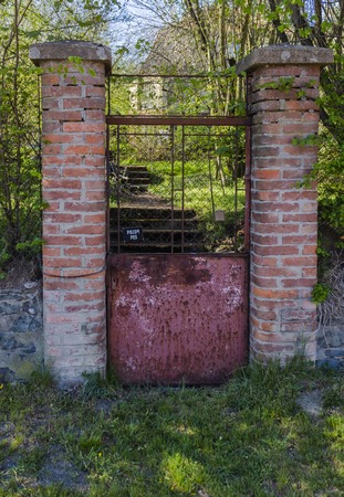 Weathered old rusty garden gate, brick wall pillars, with sign in czech, that means: Beware of Dog.の写真素材