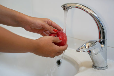 A girl washes an apple under the tapの写真素材