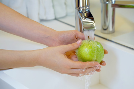 Woman young housewife washing fresh green apple in kitchen under water stream. Healthy eating.の写真素材
