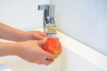 Woman young housewife washing fresh red apple in kitchen under water stream. Healthy eating.の写真素材
