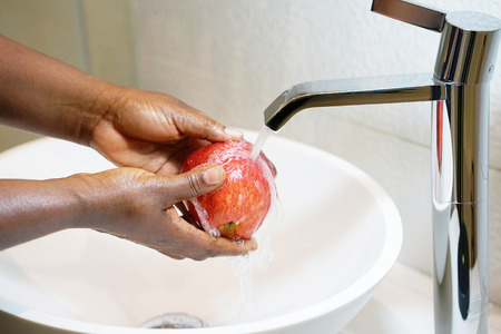 Female hands wash the apple under the tap. Woman young housewife washing fresh red apple in kitchen under water stream. Healthy eating.の写真素材