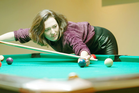 Young brunette girl playing snooker. Young happy woman having fun with billiard. Smiling fashionable woman playing spending time on recreation. Play and fun concept.の写真素材