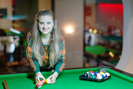 Young girl playing snooker. Young happy woman having fun with billiard. Smiling fashionable woman...