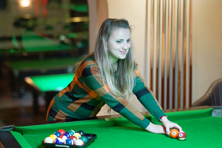Young girl playing snooker. Young happy woman having fun with billiard. Smiling fashionable woman playing spending time on recreation. Play and fun concept.の写真素材