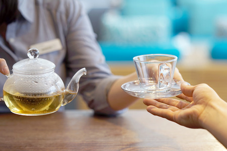 The waitress takes a cup with a tea kettle for the client at the restaurant. The concept of service and maintenance.の写真素材