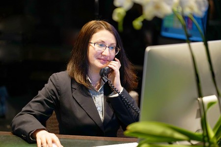 Close-up of an office worker. Woman secretary answering phone calls and talking with customers, she is sitting at her desk working.の写真素材