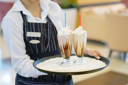 the waitress bears two vanilla milkshakes for the client of the hotel restaurant. Two chocolate dairy cocktails on a waitress tray.の写真素材