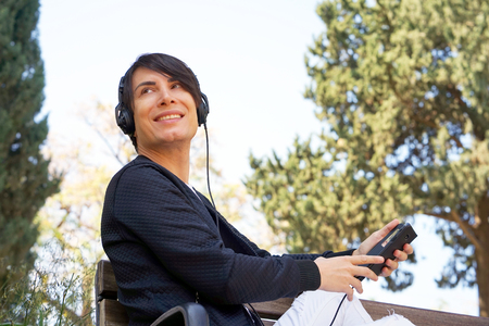 Joyful attractive guy listening to music on headphones while enjoying sitting in the parkの写真素材