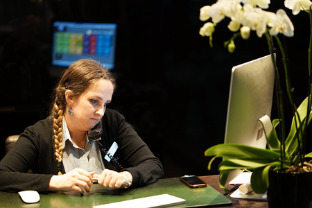 Hotel administrator. A woman-reception worker accepts an order for booking a room by phone. Profile shot of attractive executives at the reception of a hotel. The concept of service.の写真素材