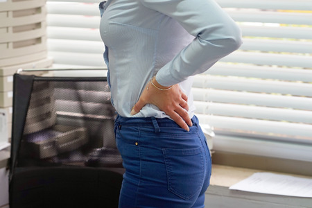 Close-up view of a office worker woman with pain in kidneys. Young woman with back ache clasping her hand to her lower back. Woman suffering from ribbing pain, waist pain.の写真素材