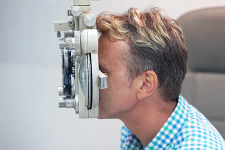 health care, medicine, people, eyesight and technology concept - man checks his vision on the machine checking patient vision at eye clinic or optics store. face close-upの写真素材