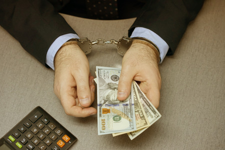 Close-up. Businessman in office in handcuffs holding a bribe. Arrested man in handcuffs. Toningの写真素材