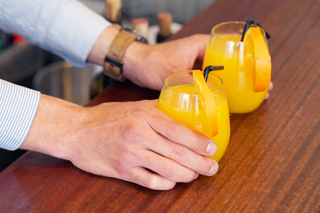 The waiter transfers the order for two orange juice to the client of the hotel bar. The concept of service.の写真素材