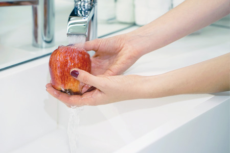 Female hands wash the apple under the tap. Woman young housewife washing fresh red apple in kitchen under water stream. Healthy eating.の写真素材