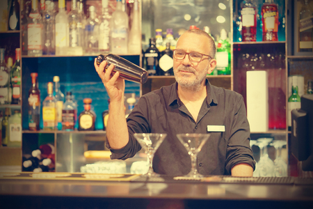 Professional bartender man holding in hands a shaker with a fresh delicious cocktail. Bartender shaking a cocktail shaker as she stands behind the bar mixing a drink for a client. Toningの写真素材
