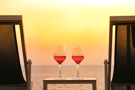 Two glasses of red wine on a background of a sea horizon in the evening. Two summer chairs and a table with two glasses of red wine at sunset. Toningの写真素材