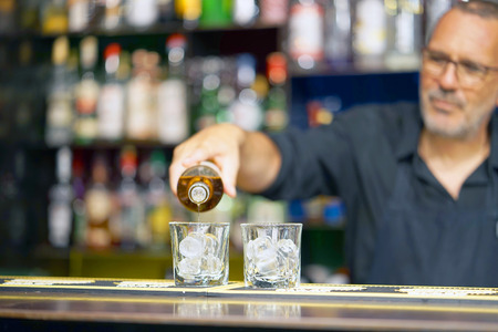 Bartender man pours whiskey to the client of the hotel bar. The concept of service. Focus on the glass.の写真素材