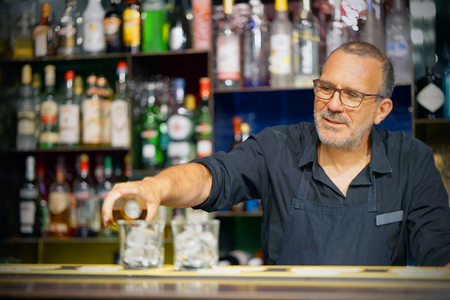 Bartender man pours whiskey to the client of the hotel bar. The concept of service. Focus on the bartender.の写真素材