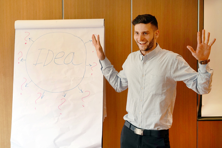 Successful smiling male coach explaining a training seminar standing next to the board with the layout area with your business information. A cheerful businessman holds a seminar in the team.の写真素材