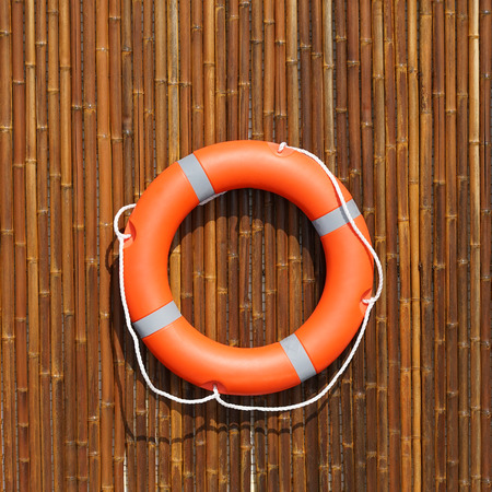 Red lifebuoy pool ring hanging on a bamboo wall for emergency response, when people submerging in the water, almost near the pool and the beach. Life ring in swimming pool.の写真素材