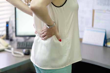 Close-up view of a office worker woman with pain in kidneys. Young woman with back ache clasping her hand to her lower back. Woman suffering from ribbing pain, waist pain.の写真素材