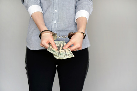 Close-up. Business woman in handcuffs holding a bribe isolated on gray background. Arrested or arrested terrorist in handcuffs. Criminal hands female locked in handcuffs. Hands in front.の写真素材