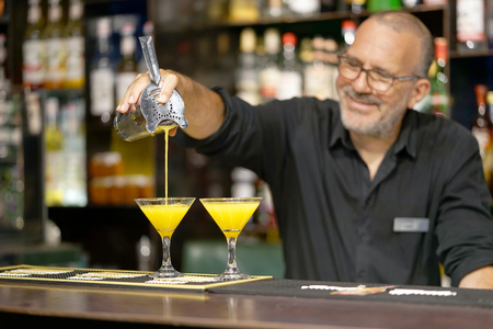 The barman pours an orange cocktail into a glass beaker. The bartender pours the cooked ingredients into a chilled cocktail at the bar. Close-up.の写真素材