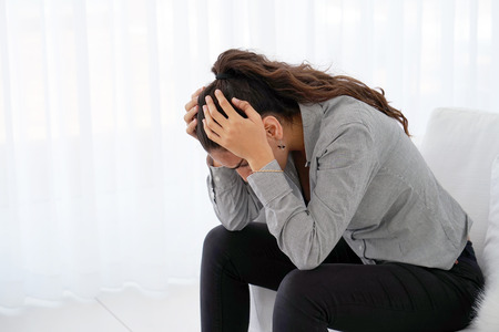 Woman suffering from headache migraine pain at home on sofa. Health problem, stress and depression. Female holds head with hand. Concept of health.の写真素材
