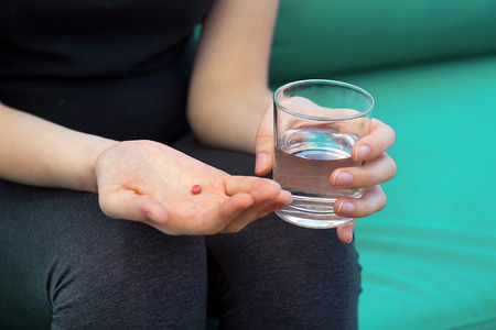 Sick woman holding pill glass of water on the sofa. Depressed unhealthy woman, about to take antidepressant pill, emergency contraceptive, painkiller for painful periods.の写真素材