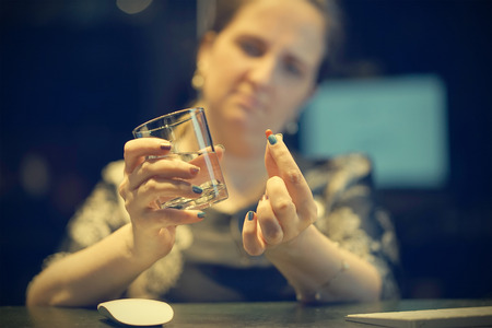 Close-up of office worker Sick woman holding pill glass of water. Depressed unhealthy woman, about to take antidepressant pill, emergency contraceptive, painkiller for painful periods. Toningの写真素材