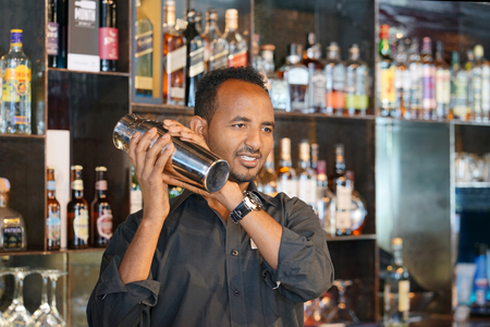 Professional bartender man holding in hands a shaker with a fresh delicious cocktail. Bartender shaking a cocktail shaker as she stands behind the bar mixing a drink for a client. Close-up.の写真素材