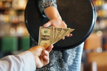The hand of the waitress takes the tip. The waiter girl receives a tip from the client at the hotel bar. A bartender woman is happy to receive a tip at work. The concept of service.の写真素材
