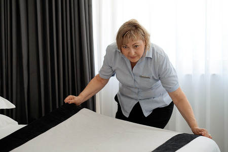 Maid making bed in hotel room.の写真素材