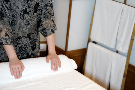 The girl prepares a workplace massage bed in the spa for the reception of clients. The maid is preparing a room for the spa salon. Woman masseuse in the workplace. The concept of health and beauty.の写真素材