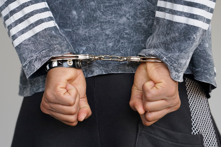 Close-up. Arrested man handcuffed hands at the back isolated on gray background. Prisoner or arrested terrorist, close-up of hands in handcuffs.の写真素材
