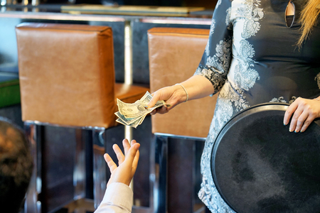 The hand of the waitress takes the tip. The waiter girl receives a tip from the client at the hotel bar. A bartender woman is happy to receive a tip at work. The concept of service.の写真素材