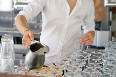 The barman pours a drink into the glass. bartender pouring juice from a pitcher iron. The concept of service.の写真素材