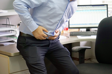 Close-up of office worker having painful stomachache. Chronic gastritis. Businessman with abdominal pain at his workplace in the office. Body And Health Care Concept.の写真素材