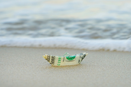 A boat made of paper money in the sea sand A boat out of the dollar in the sea. Sea sand. Concept...