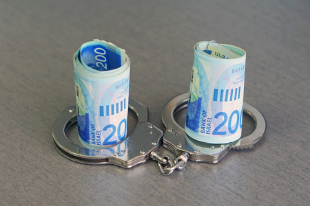 roll Israeli money bills (banknotes) of 200 shekel in handcuffs. Shekel bills with handcuffs. Handcuffs and money on table. Financial crime, dirty money and corruption concept. Tax offense conceptの写真素材