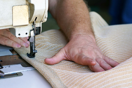 Men's hands sew bags on the sewing machine. Sewing bags for rice and sugar. Hired labor. Professional seamstress. Man seamstress. Men's hands behind sewing leather.の写真素材
