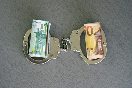 roll Euro money bills (banknotes) of 100 and 50 in handcuffs. Euro bills with handcuffs. Handcuffs and money on table. Financial crime, dirty money and corruption concept. Tax offense concept.の写真素材
